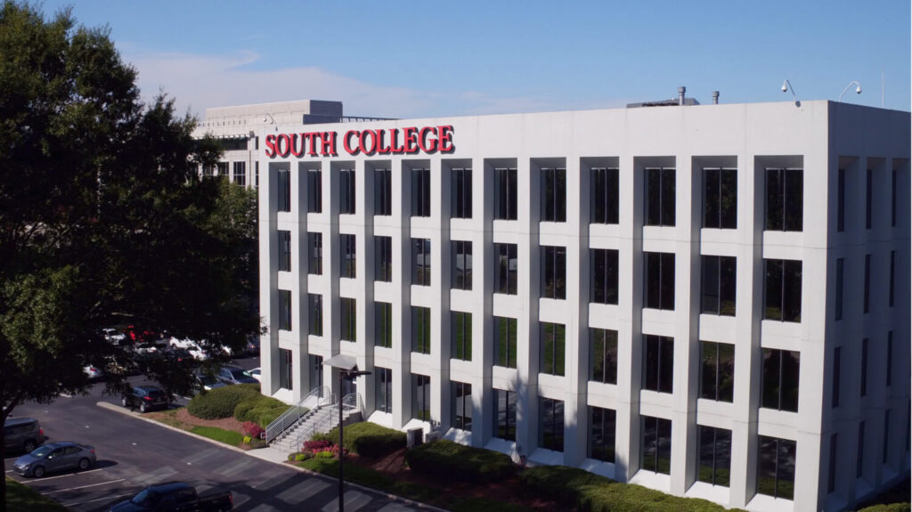 A four-story building with white exterior, many windows, and large red letters on top spelling "South College."