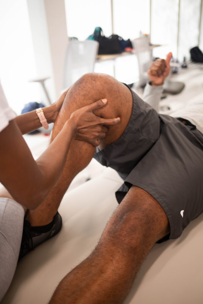 A person lying on a clinic bed receives physical therapy from a South College student.