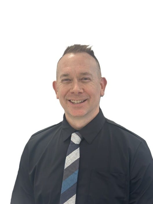 A smiling man with short, styled hair wearing a black dress shirt and a striped tie stands against a plain white background.